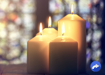 trio of lit candles with stained glass in background