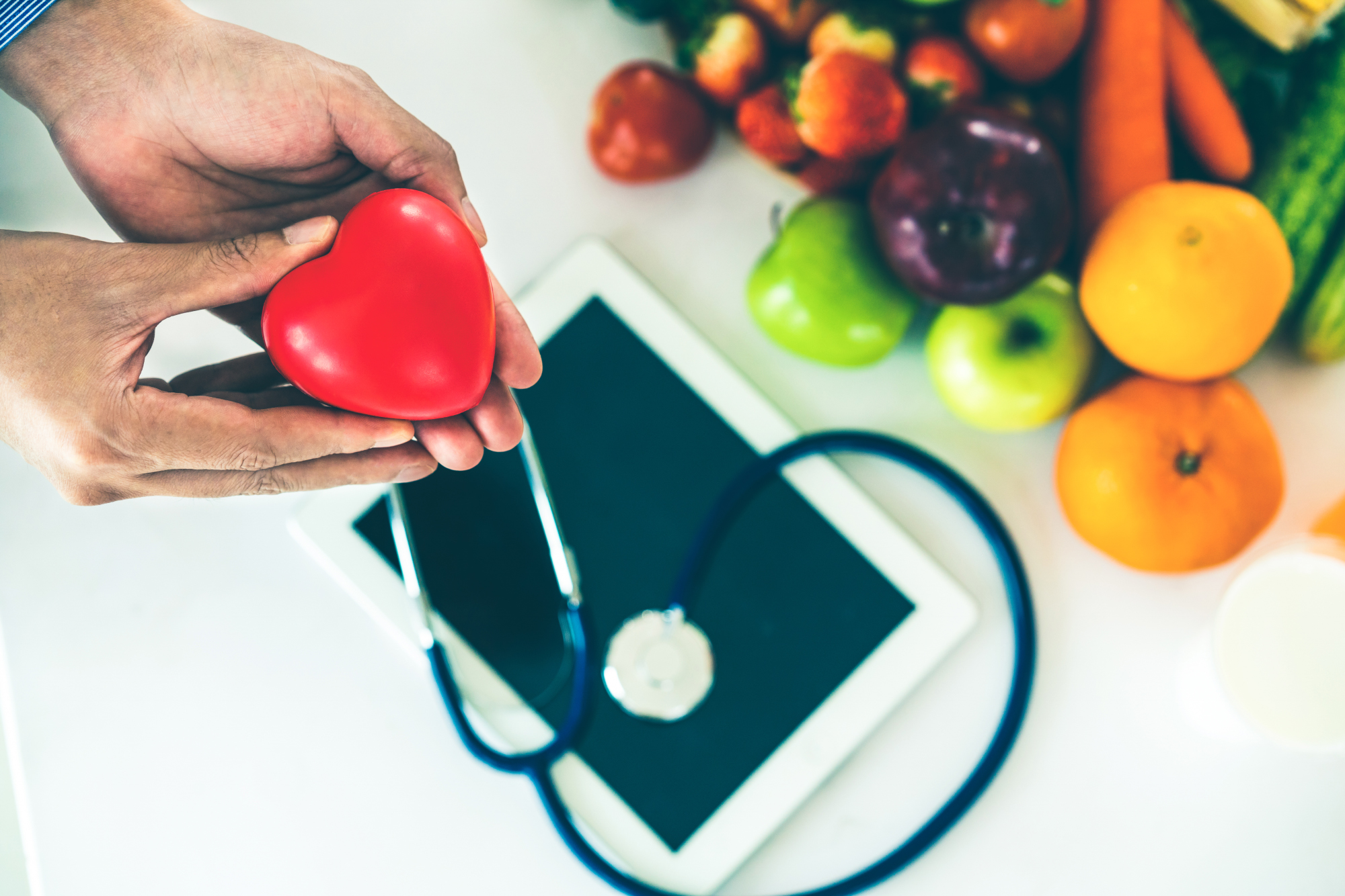 hands holding heart above stethescope and healthy food