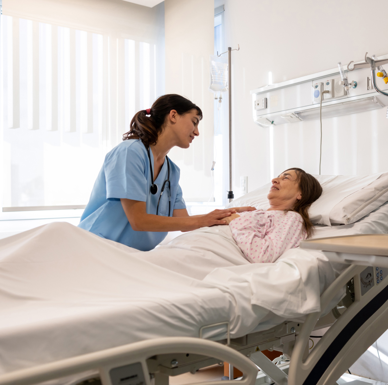 A nurse caring for an elderly patient lying in a hospital bed