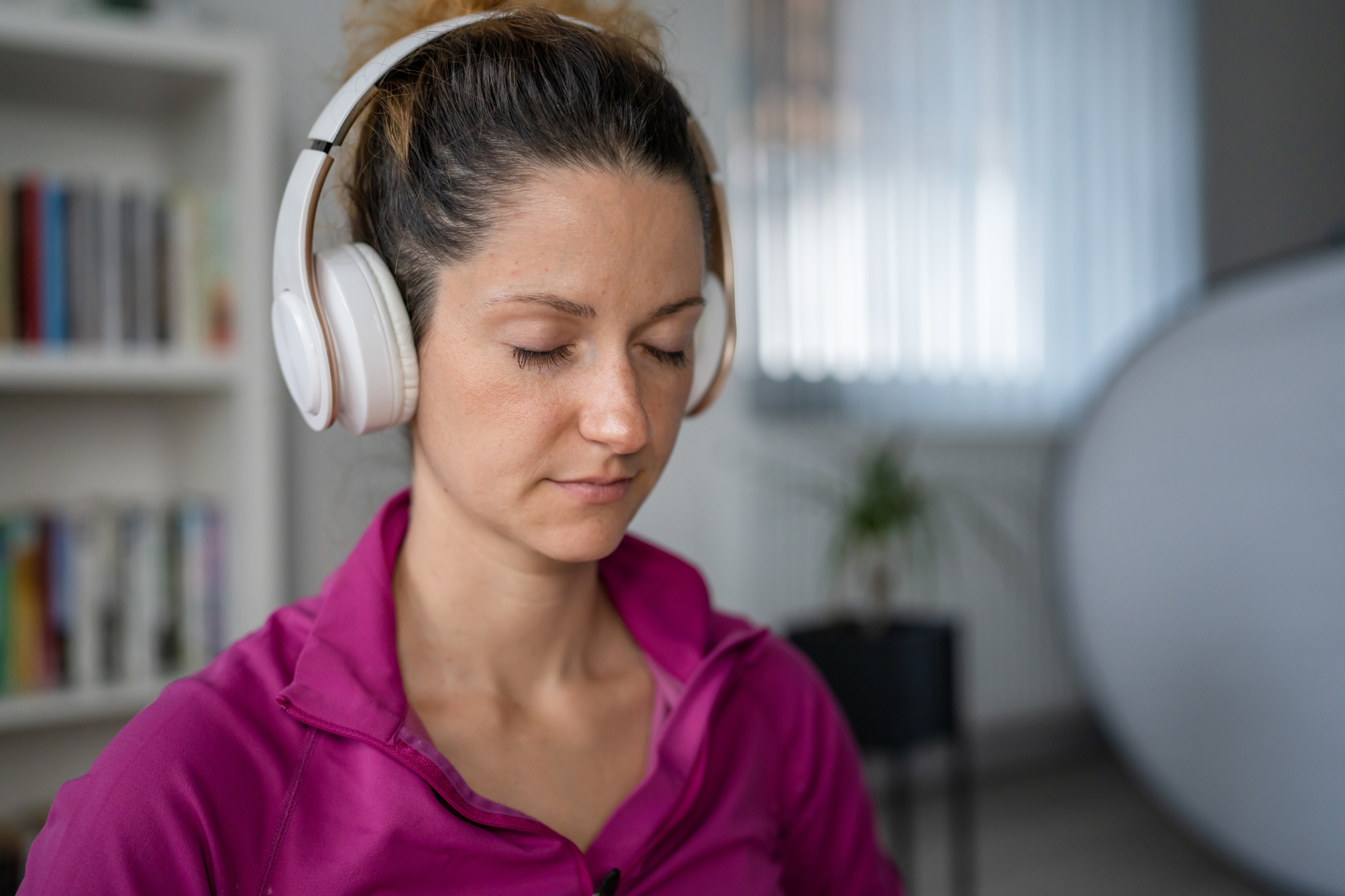 A woman wearing headphones, with her eyes closed, appearing relaxed.