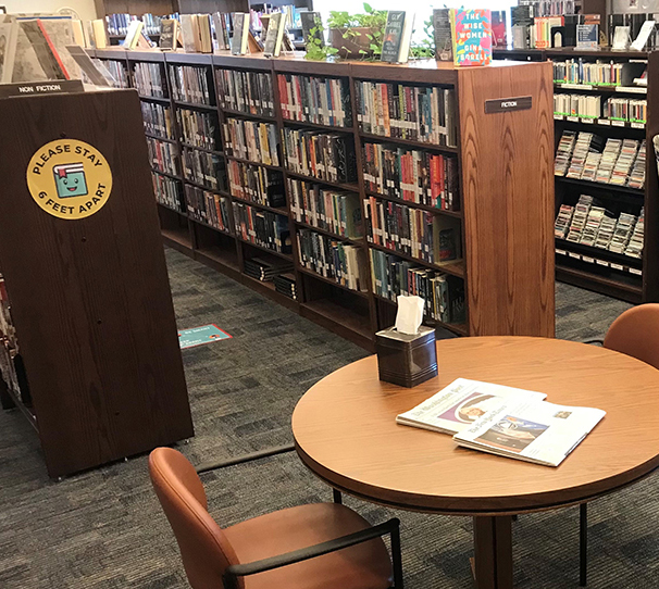 A table with an open book with rows of bookshelves in the background.
