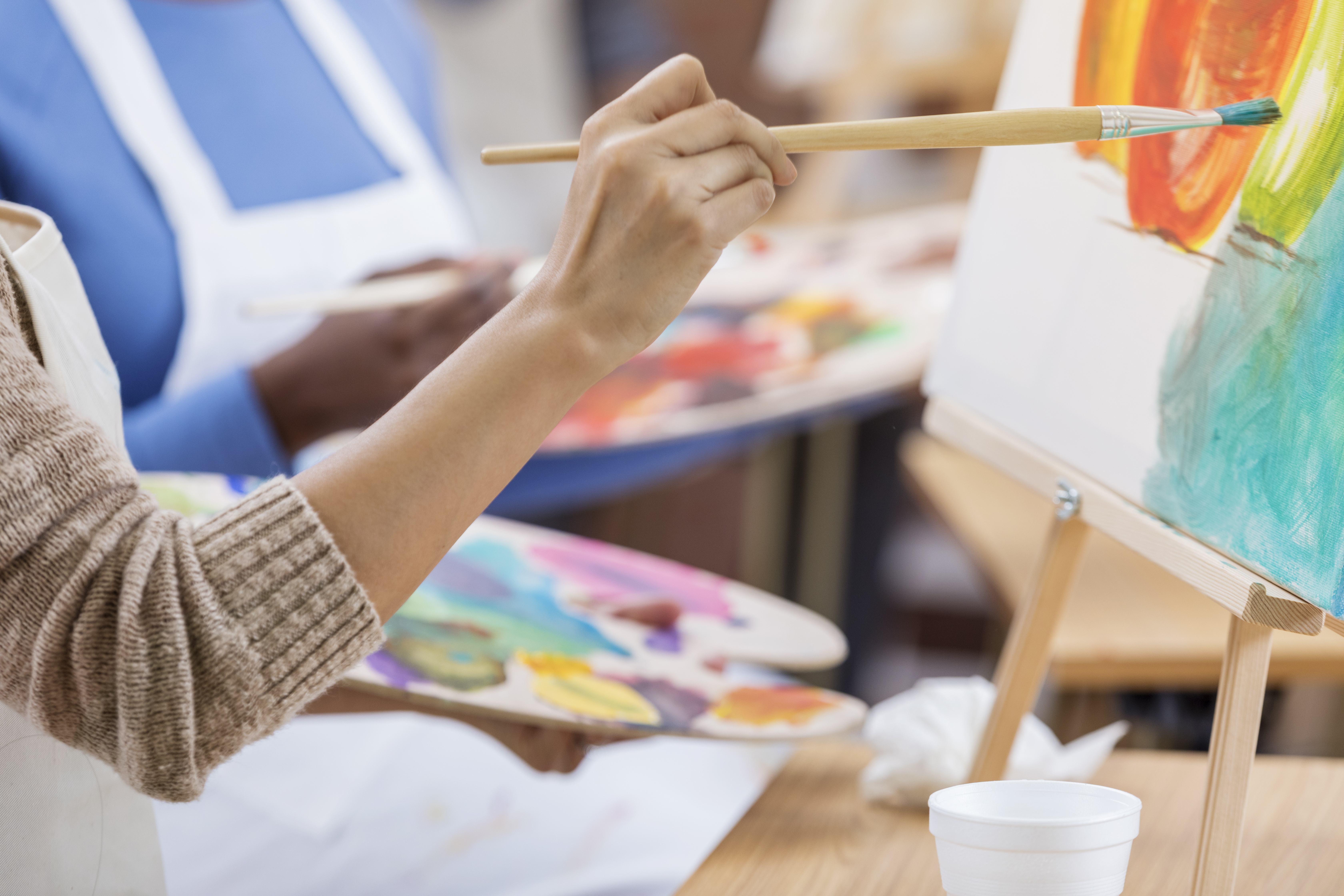 An artist uses a paintbrush to add vibrant colors to a canvas during a painting session, with a palette of mixed paints in the other hand.