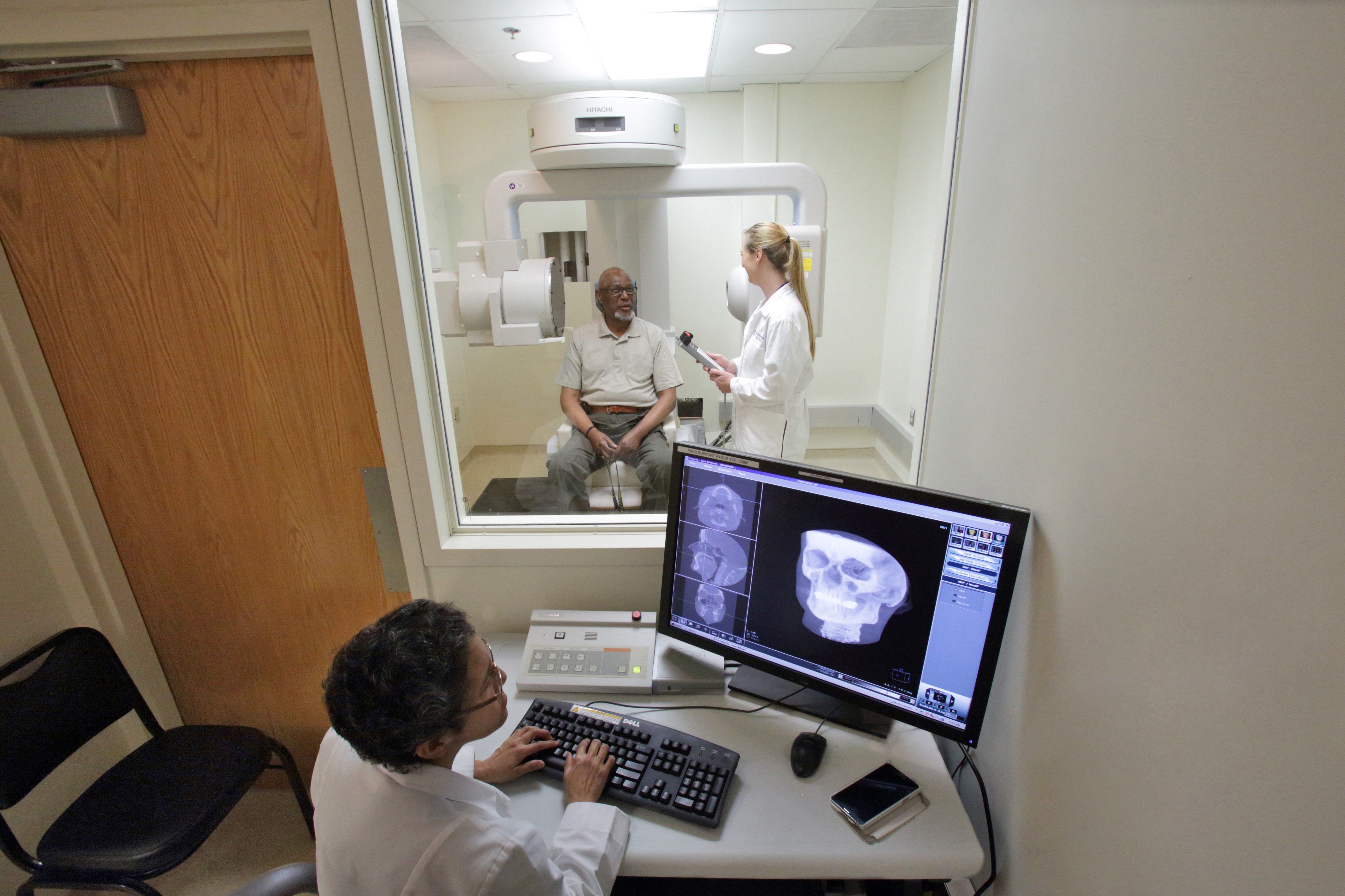 Patient receiving CT scan while researcher reviews the scan in another room